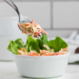 a forkful of creamy cole slaw out of a white bowl